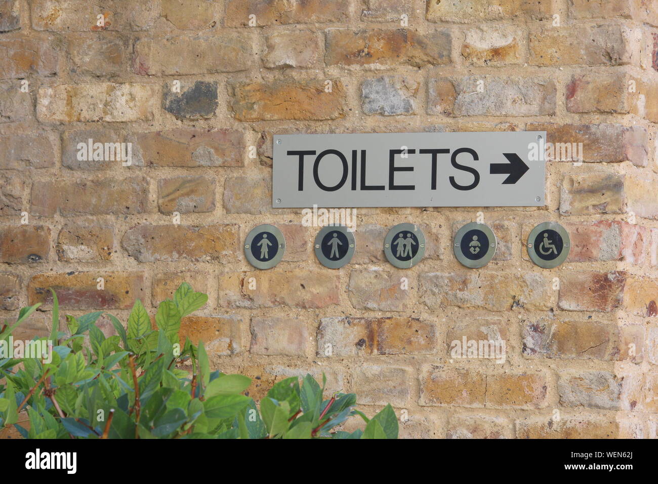 A photograph of a metal toilet sign, men's, women's, disabled, gender neutral, baby changing. Metal sign on a stone wall. Stock Photo