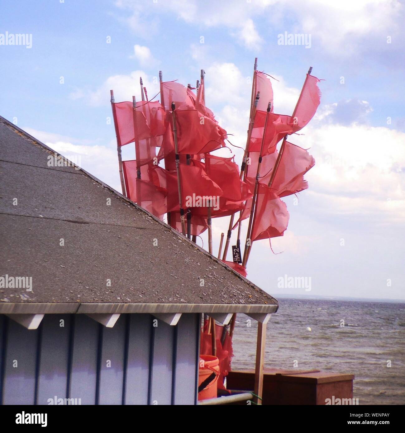 Scenic View Of Red Flags In Wind By Hut Against Sky Stock Photo
