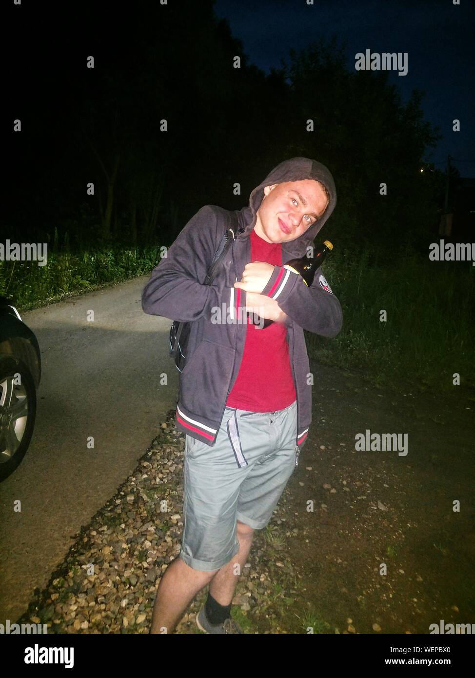Portrait Of Smiling Man In Hood Clothing Standing On Footpath At Night Stock Photo