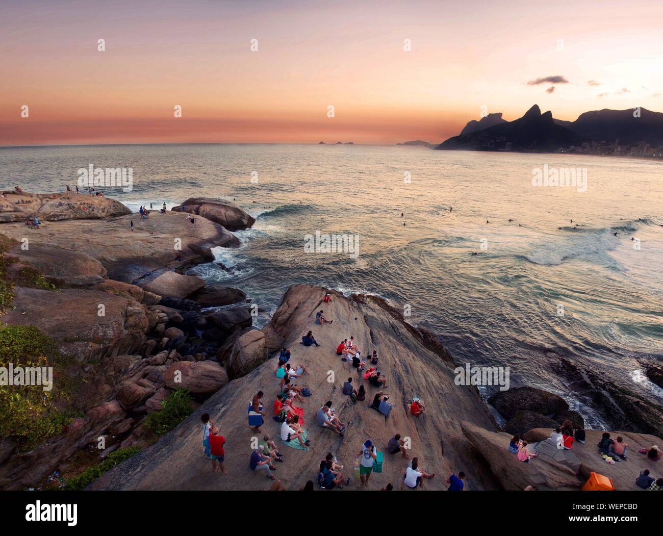 High Angle View Of People On Rock Formations By Sea At Arpoador During Sunset Stock Photo