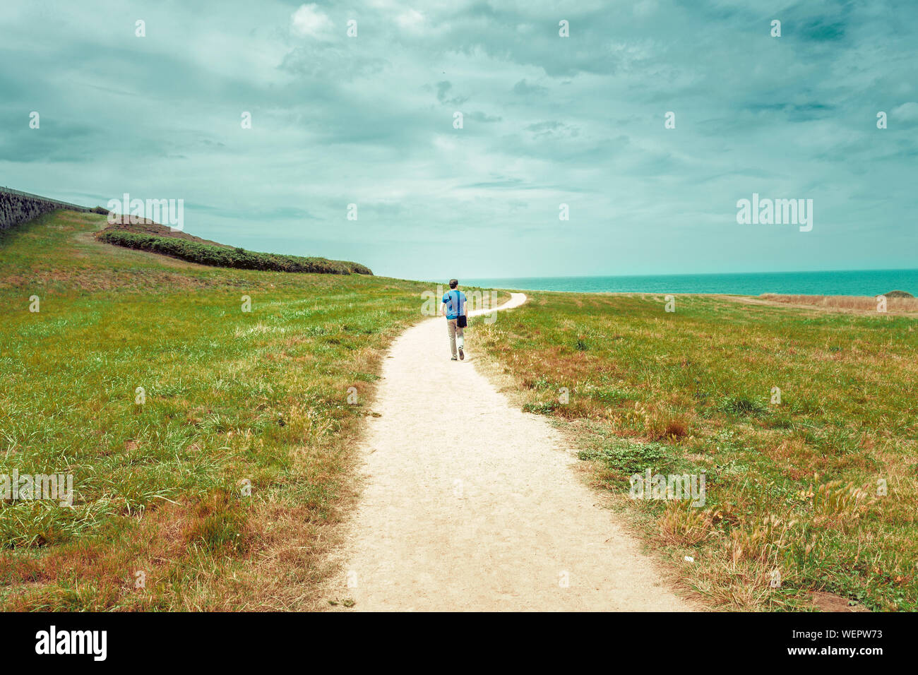 solitary man walking on a lonely dirt road to the sea Stock Photo