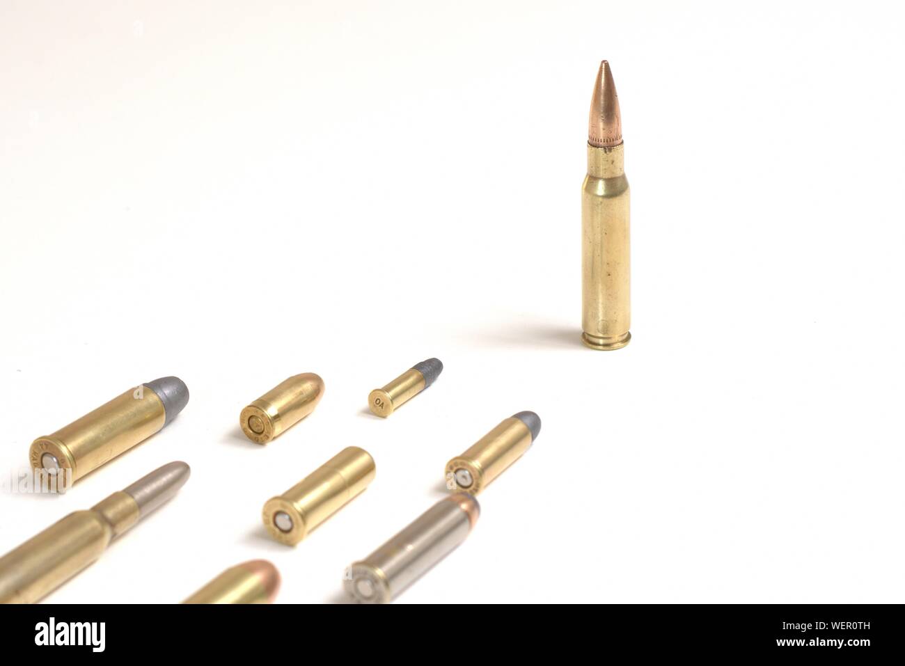 Large bullet leading several smaller bullets laying over a white surface. It works as a concept for leadership, crime, arms race. Stock Photo