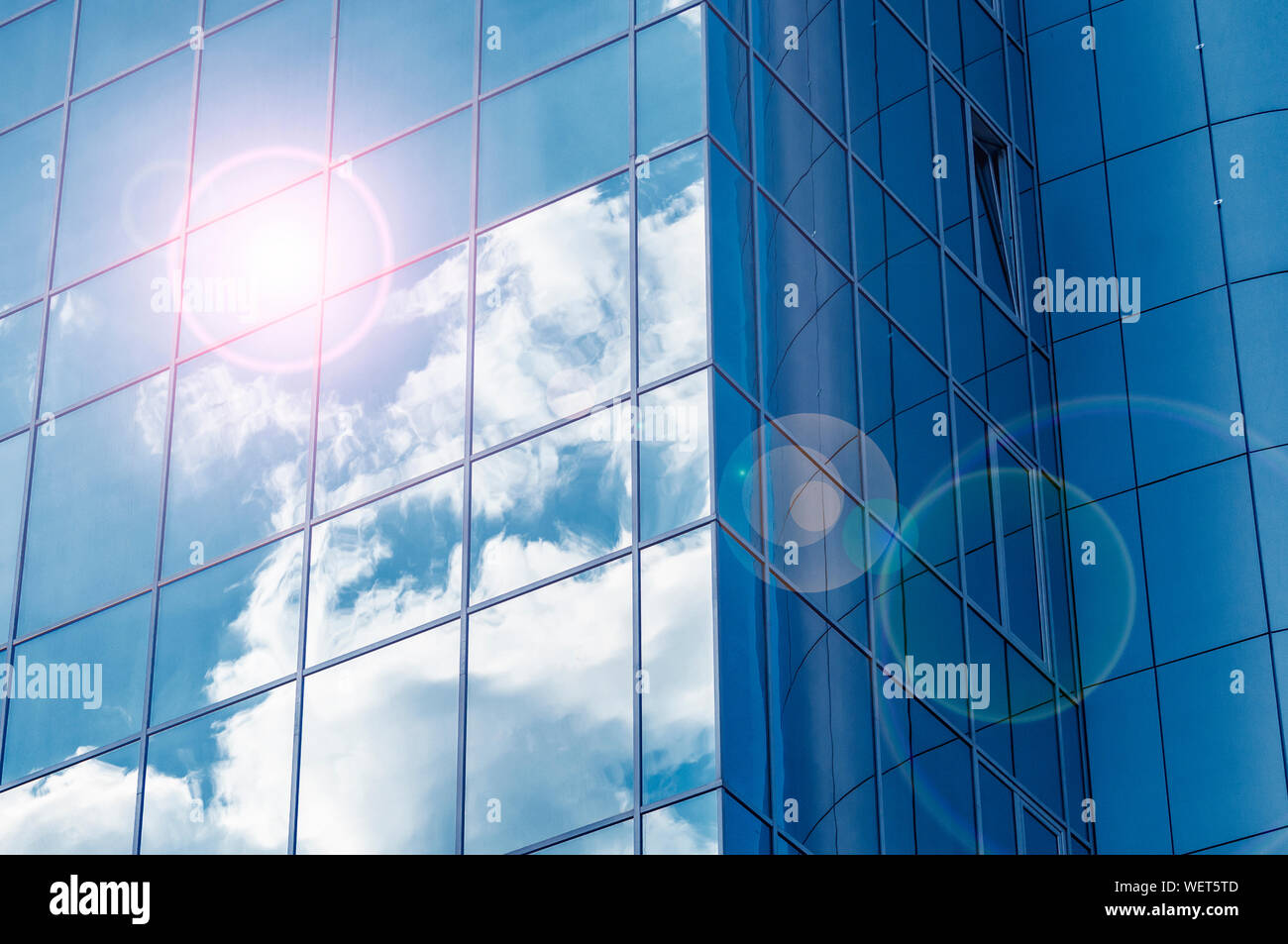 Glass windows of modern building with reflecting blue sky and clouds