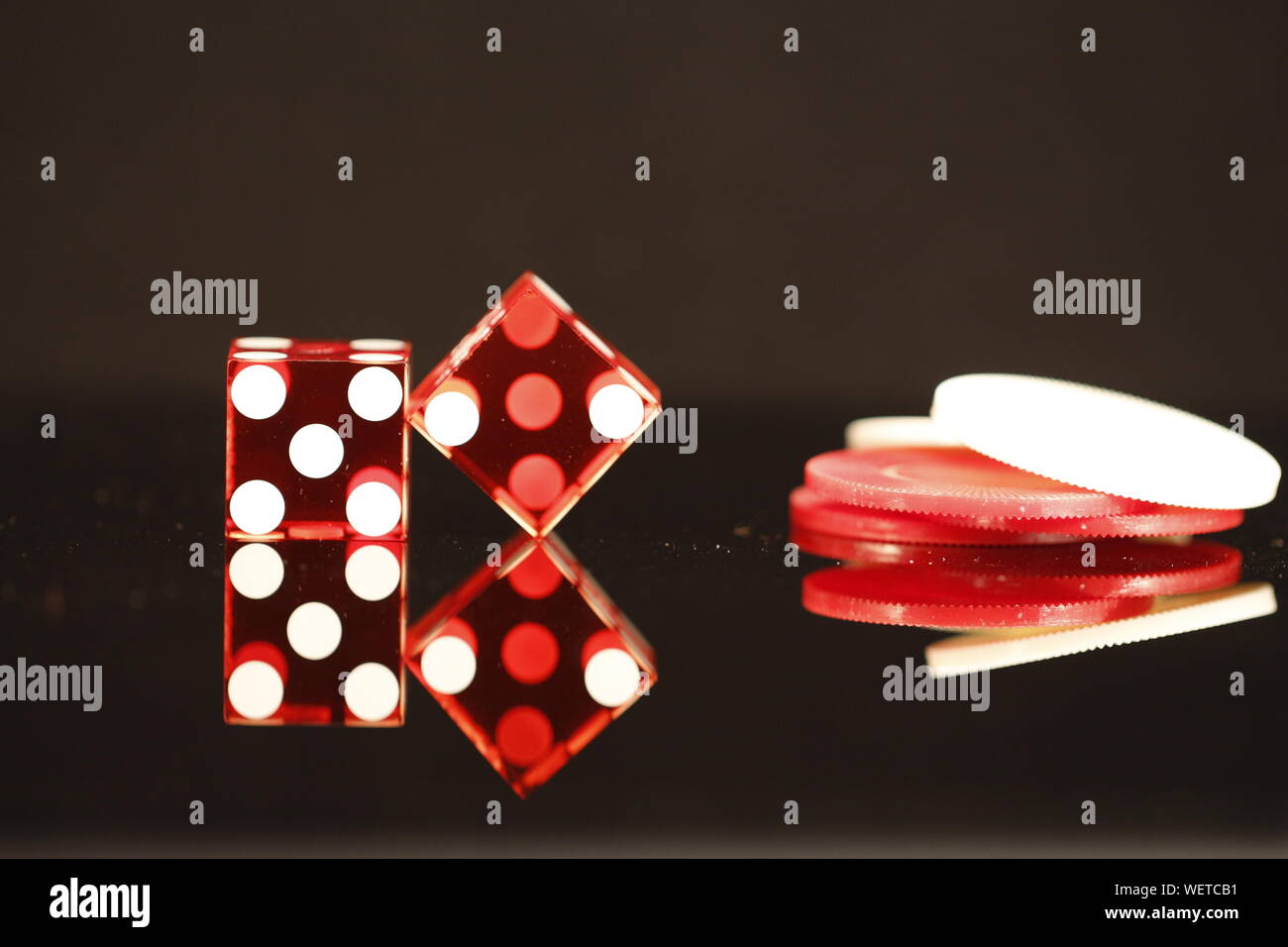 Two Red dice equaling 7 with red and white poker chips on a black reflective background Stock Photo