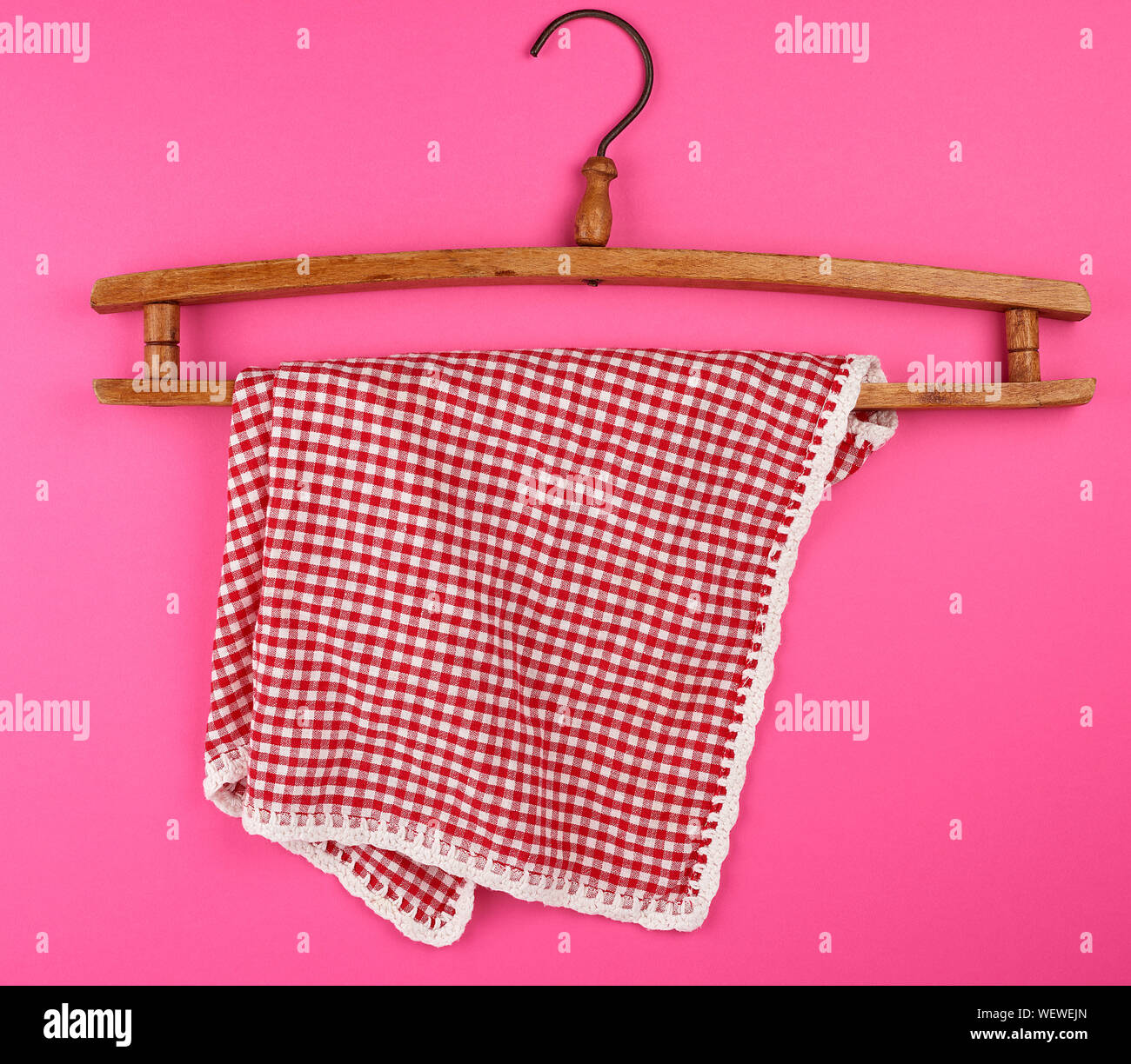 red checkered kitchen towel hanging on a vintage wooden hanger, pink background Stock Photo