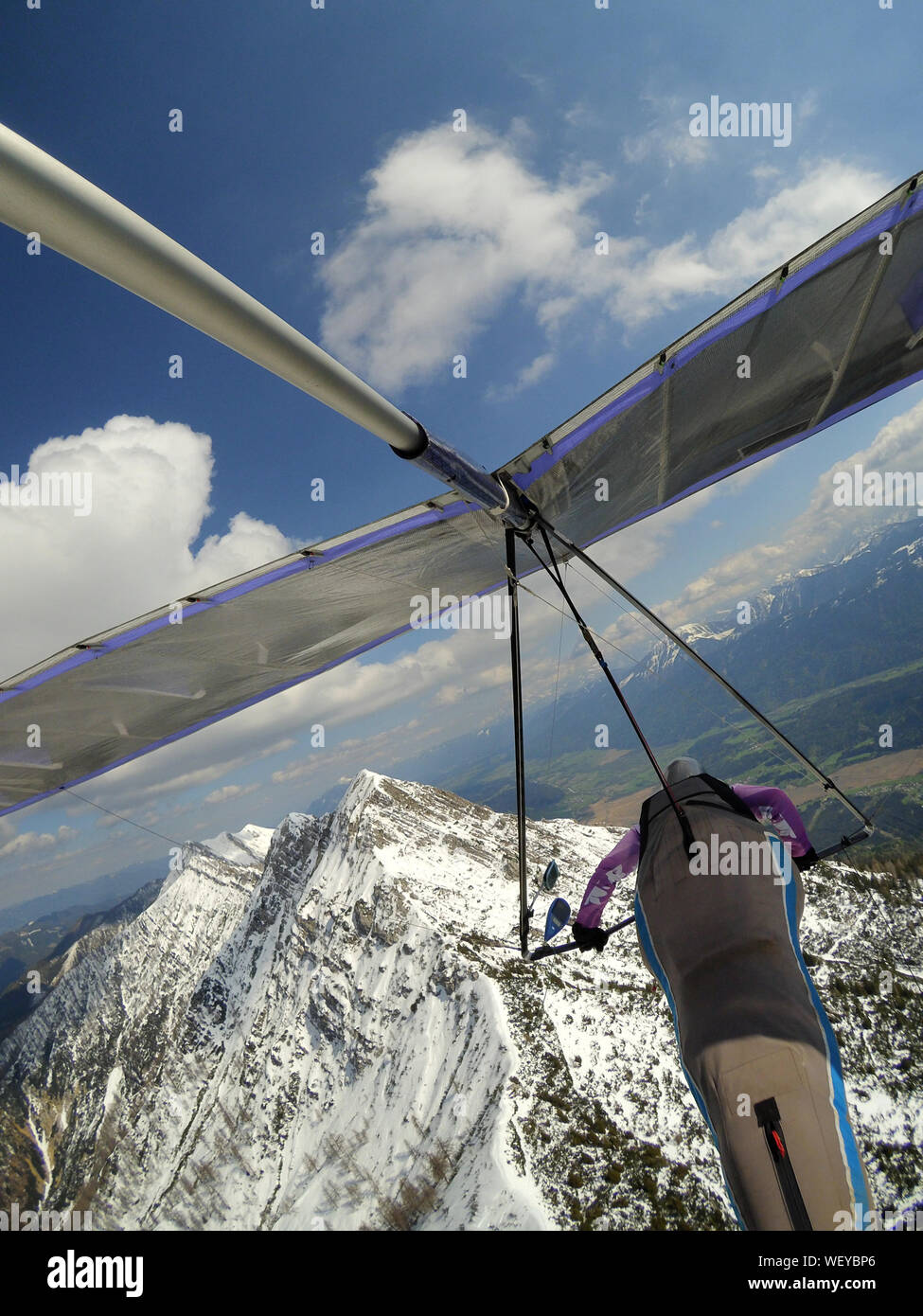 Brave pilot fly over mountain peak cobered by snow on a hang glider. Extreme aerial sport. Hang gliding Stock Photo