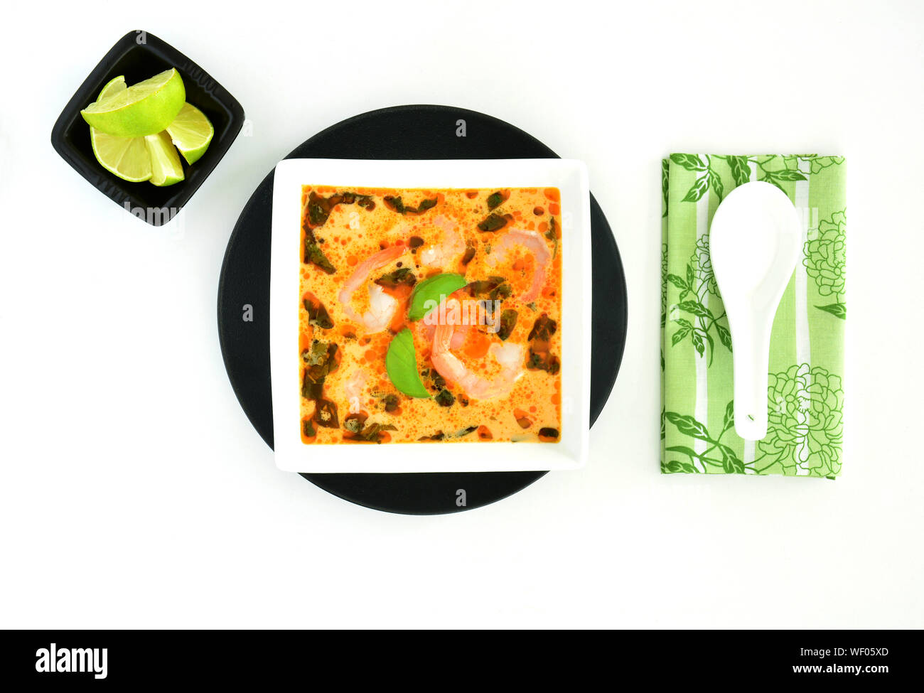 Flavourful homemade Thai coconut curry soup with shrimp in black and white dishes from overhead on white background.  Healthy eating concept. Stock Photo