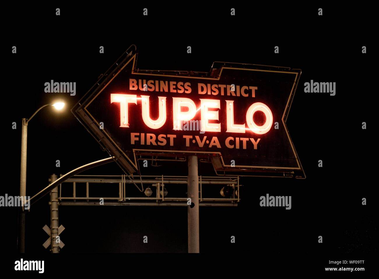 Old neon sign at night with arrow pointing towards the Tupelo, business District, with slogan, 'First TVA City', at railroad crossing in Tupelo, MS Stock Photo
