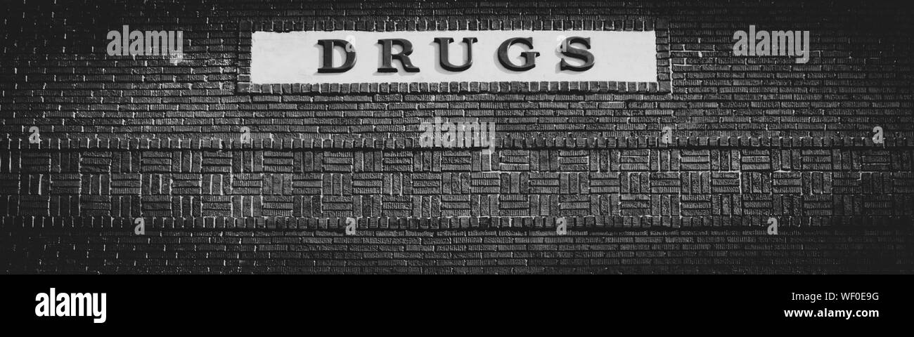 Panoramic close-up of signage on a textural vintage brick building reading DRUGS, from a bygone era pharmacy, in black and white Stock Photo