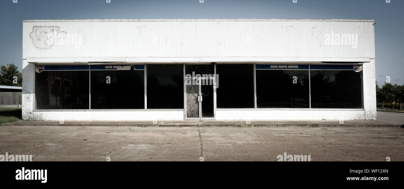 Abandoned old white commercial building in distress, once an Auto Parts center, in an empty parking lot, in an economically depressed area of America Stock Photo
