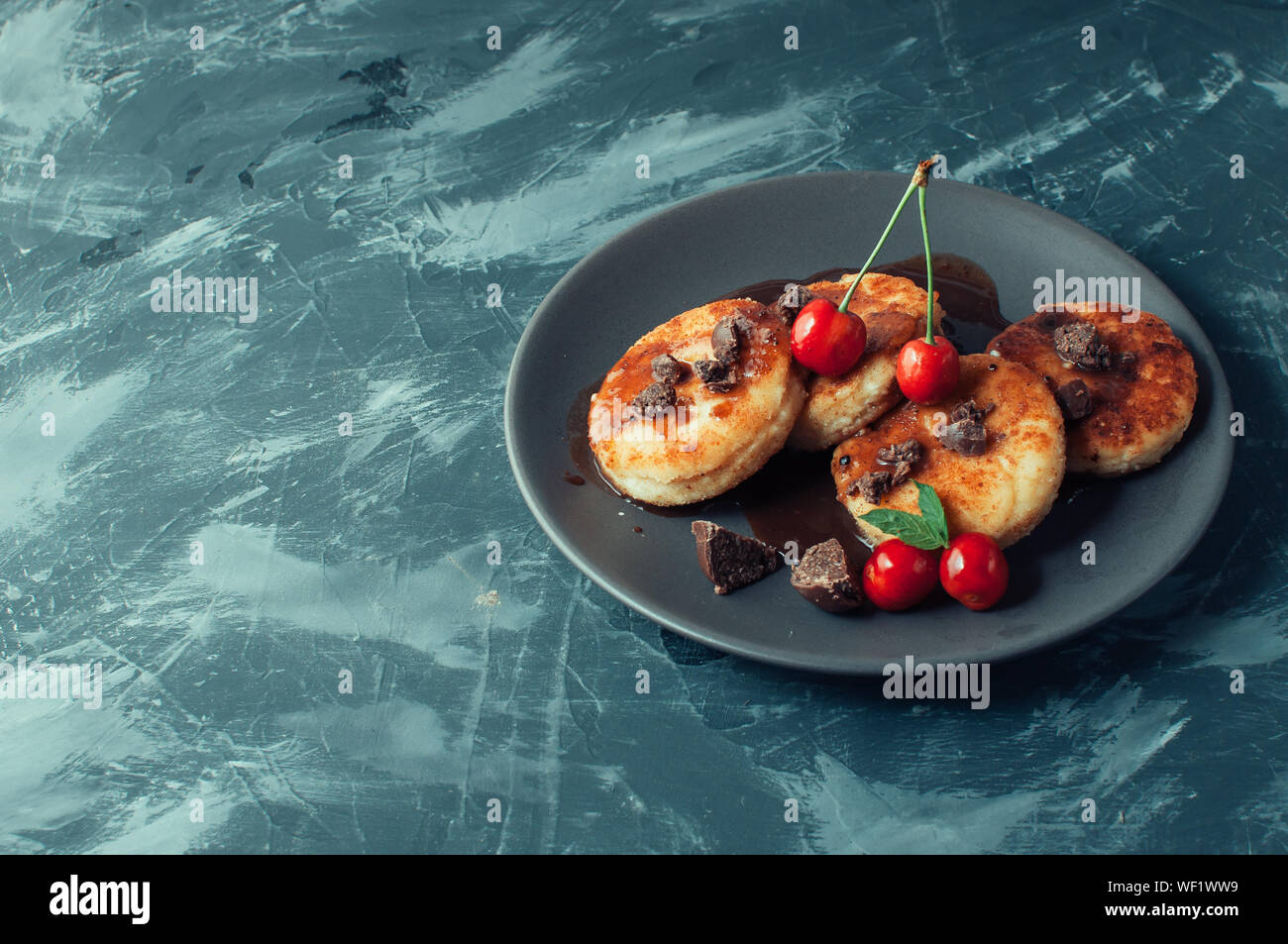 Breakfast Food Tasty Concept. Cheesecakes, cheesecakes, cottage cheese pancakes with cherries and chocolate on a black background concrete table. Clos Stock Photo