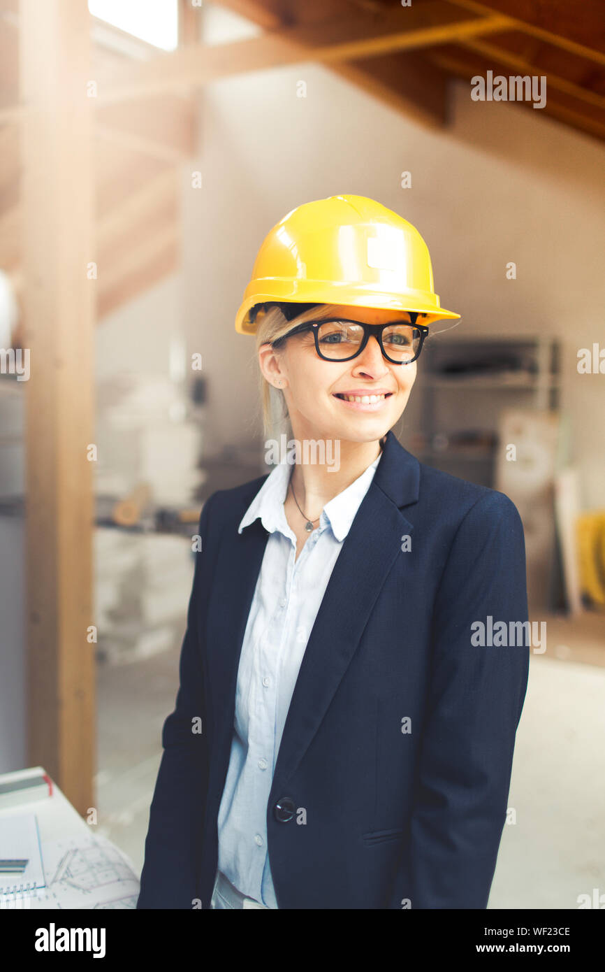 very pretty young female architect wearing yellow helmet is planning a loft in a house Stock Photo