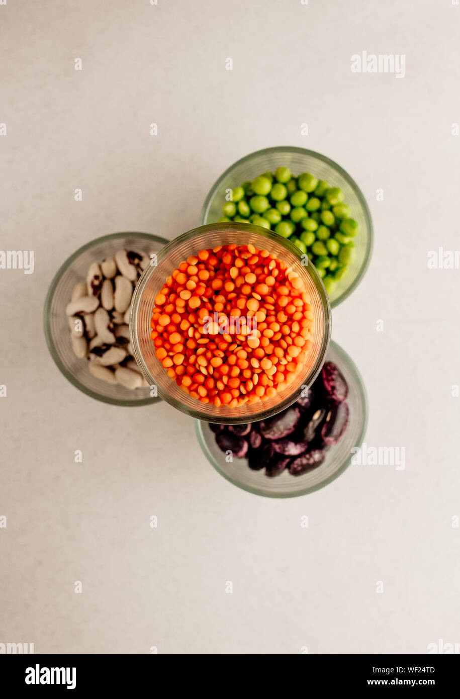 Collection set of various dried legumes in glass glasses stand in a pyramid: green peas, red beans, white beans close-up on a white background. Select Stock Photo