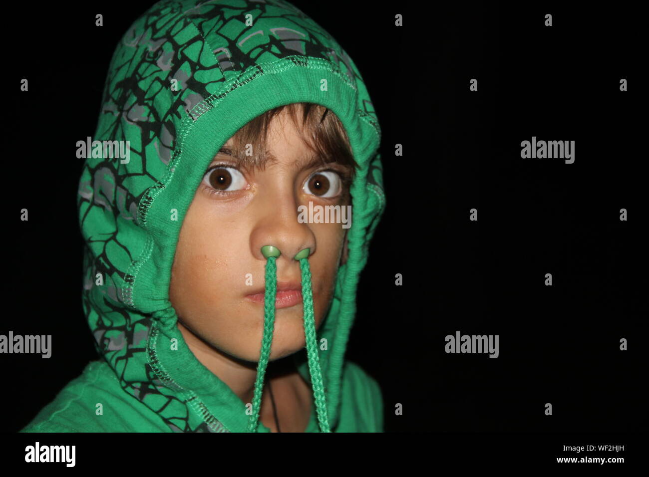 Portrait Of Playful Teenage Boy Wearing Green Hooded Shirt Against