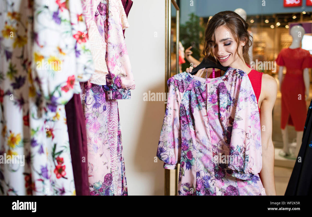 Enthusiastic smiling brunette in red trying on a flowery dress in a boutique Stock Photo