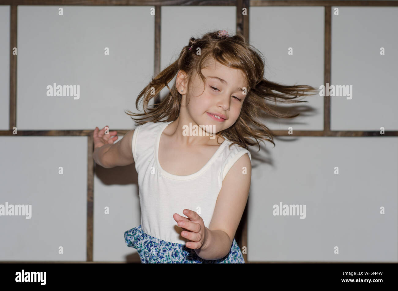 Excited Girl With Tousled Hair Jumping Against Wall At Home Stock Photo
