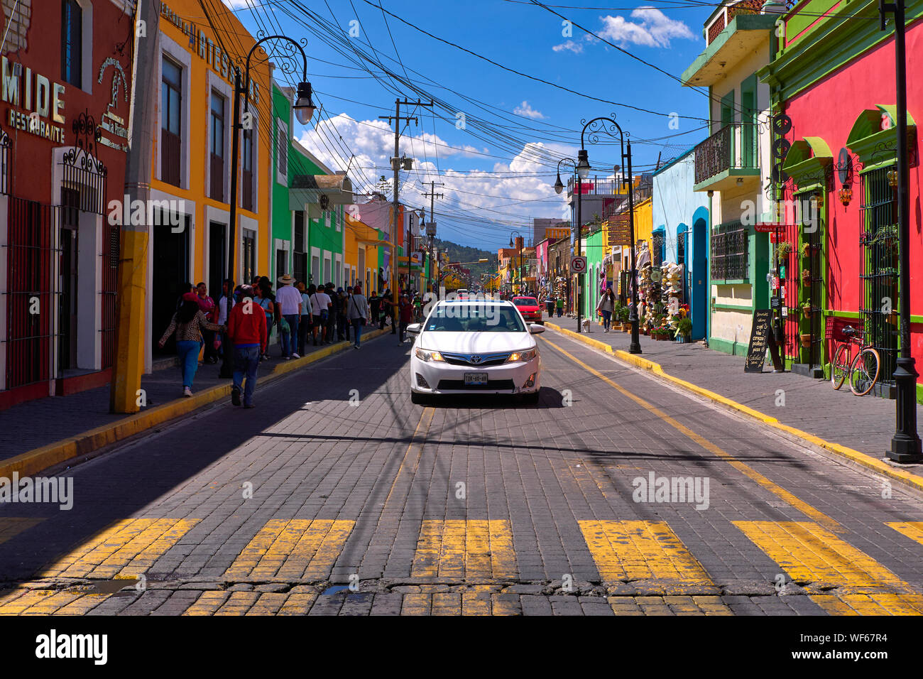 San Pedro Cholula, Mexico, September 30, 2019 - Avenida Morelos street of Cholula with tourists and cars at sunny day, traditional clothing and souvenir shops with vibrant colored facades. Stock Photo