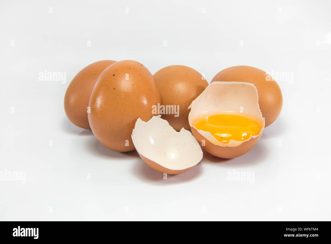 Close-up Of Brown Eggs With Broken Eggshell Against White Background Stock Photo