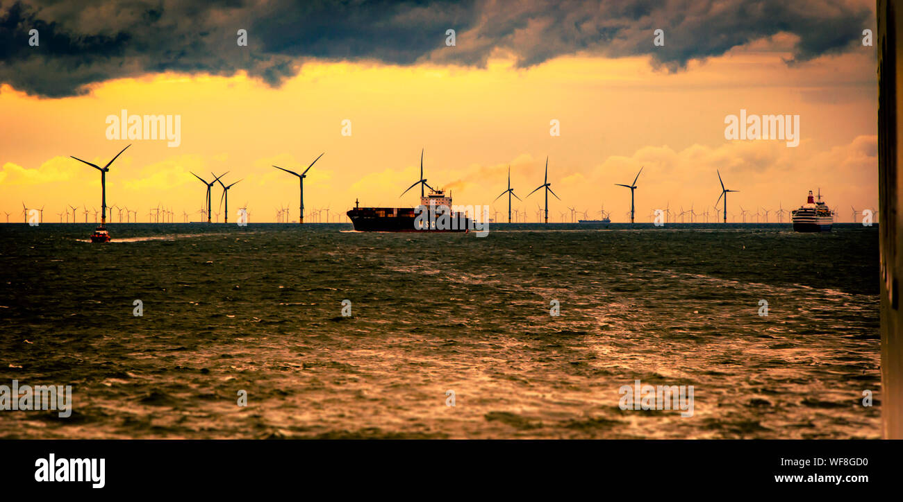 LIVERPOOL/UK, AUGUST 21, 2019: Container ship and cruise liner in shipping lane in Mersey Estuary with wind turbines and gloomy sky in background Stock Photo