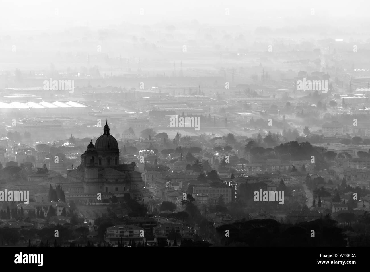 An epic, aerial view of Santa Maria degli Angeli church (Assisi)projecting sunrays, and lighting up half of the valley Stock Photo