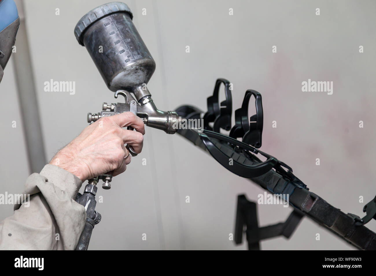 A Male Worker In Jumpsuit And Mask Paints With A Spray Gun A