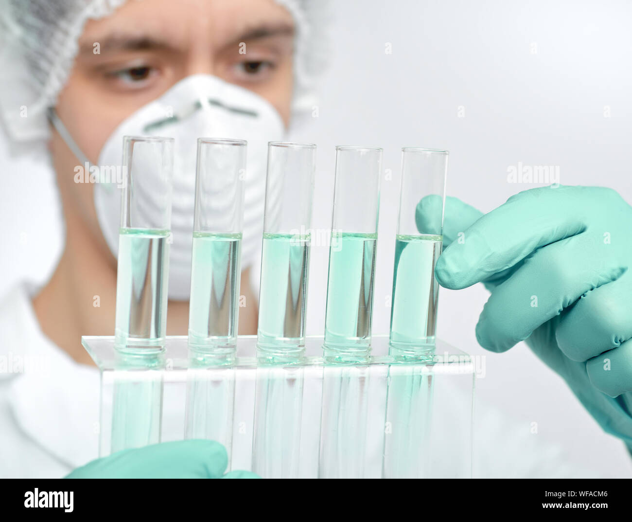 Keen adult male scientist in white gown and protective gloves holding glass tubes with chemical reaction assay. Shallow DOF, focus on the tubes, scien Stock Photo