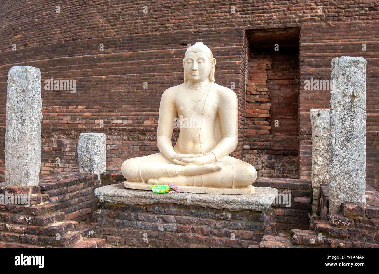 A seated Buddha statue sits in front of a section of the red brick Sandagiri Stupa at Tissamaharama in Sri Lanka. Stock Photo
