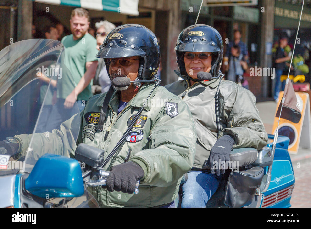 A senior couple ride on a large motorcycle through a market street with smile on their faces at Pike Place Market, Seattle, Washington, USA. Stock Photo