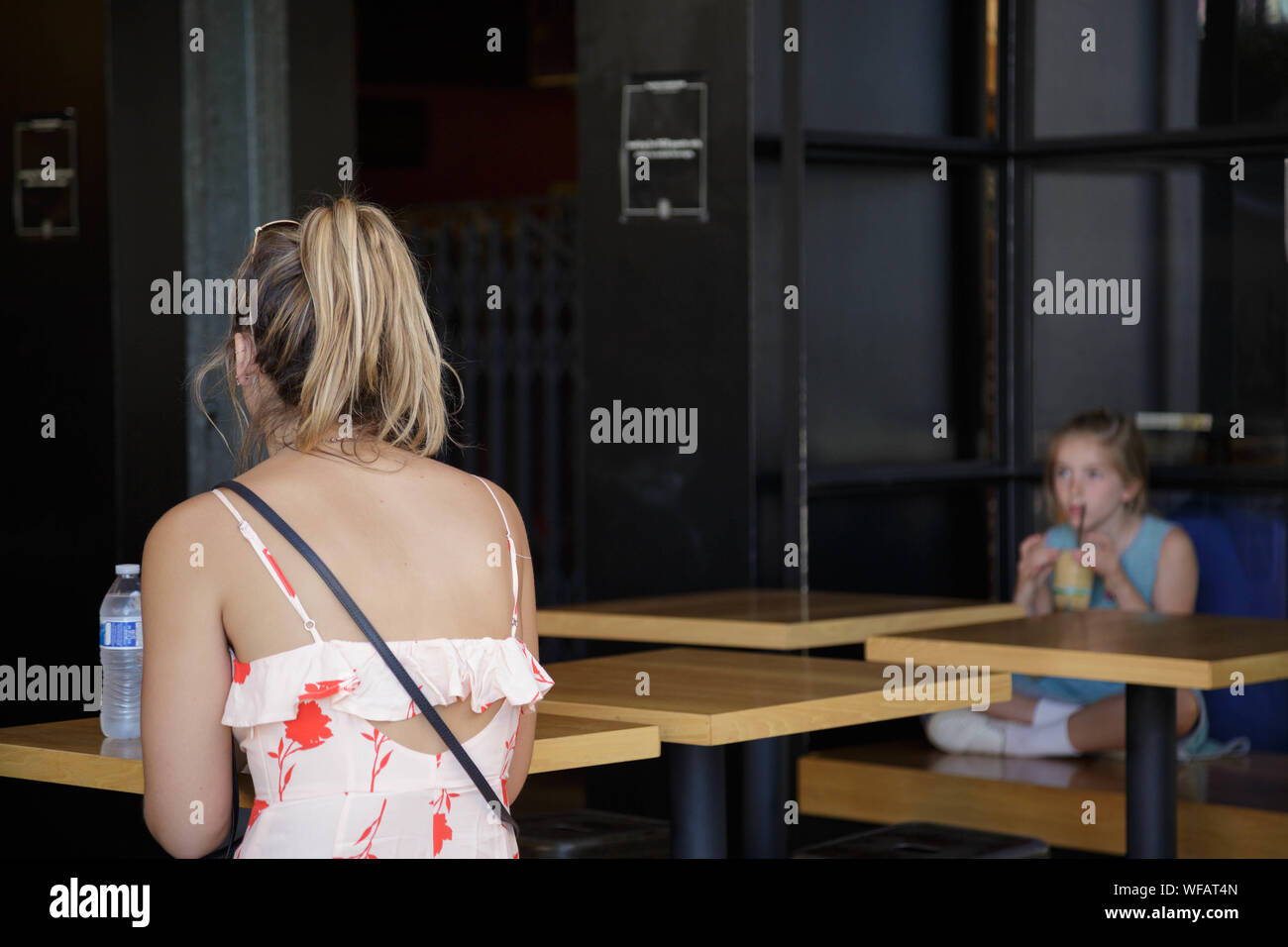 At the cafe,a blond haird woman in strap dress seated at the table alone,  in distance, a little girl drinking juice by herself Stock Photo - Alamy