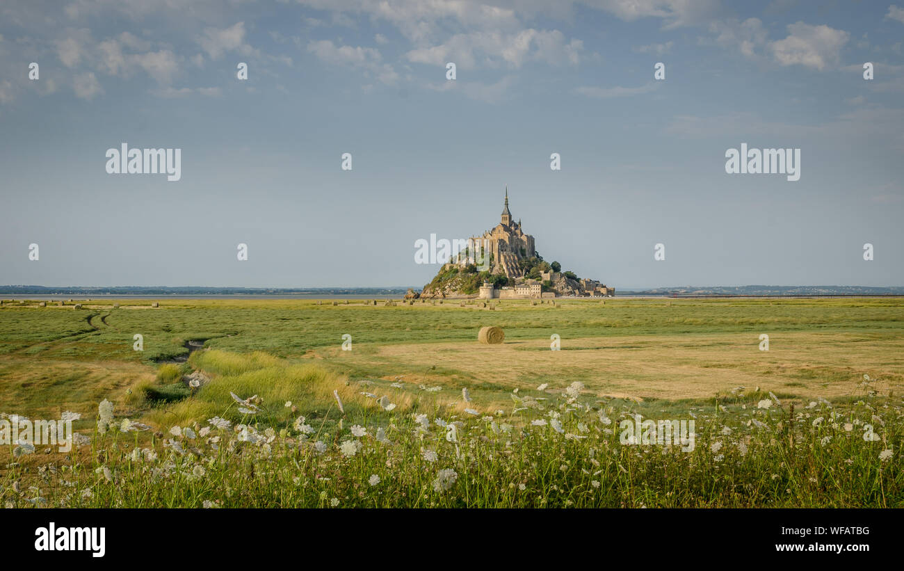 Beautiful panoramic view of famous Le Mont Saint-Michel tidal island with deep blue water and clear reflections in golden evening light at sunset in s Stock Photo