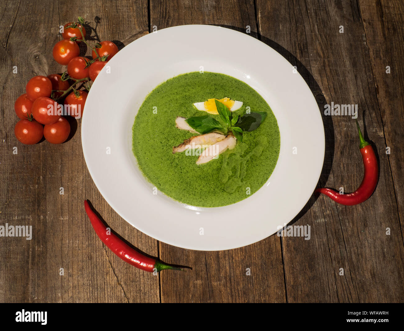High Angle View Of Spinach Creamy Soup With Cherry Tomatoes And Red Chilies Stock Photo