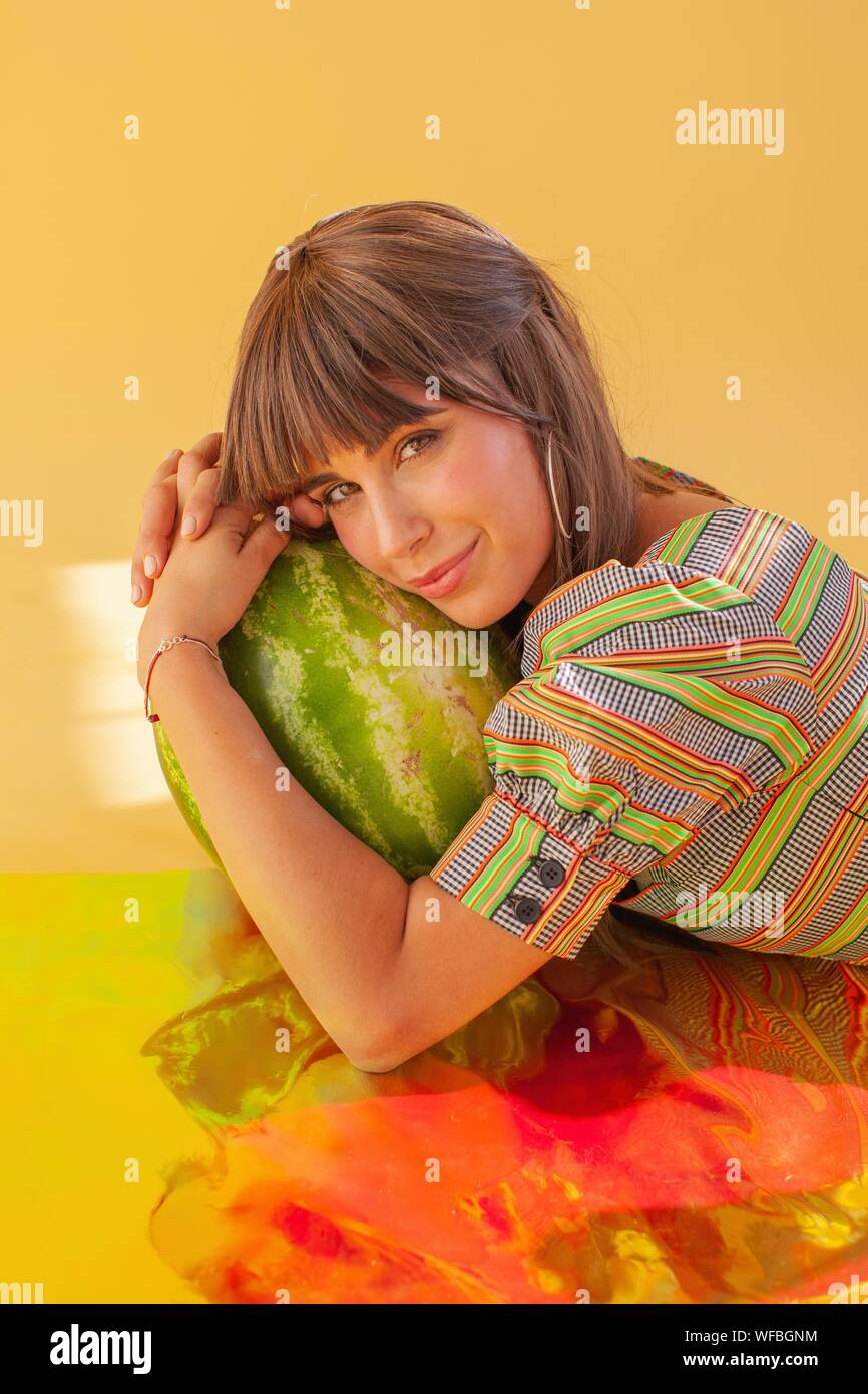 Portrait of a smiling woman lying on holographic foil holding a watermelon Stock Photo