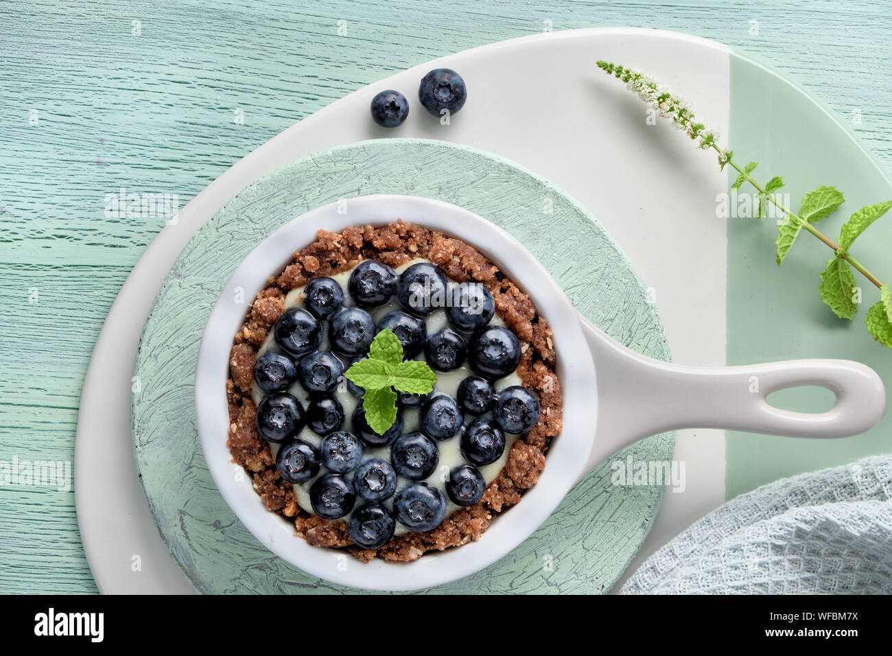 Flat lay of delicious Blueberry tartlet with vanilla custard cream and mint leaf on mint colored crackle wooden background Stock Photo