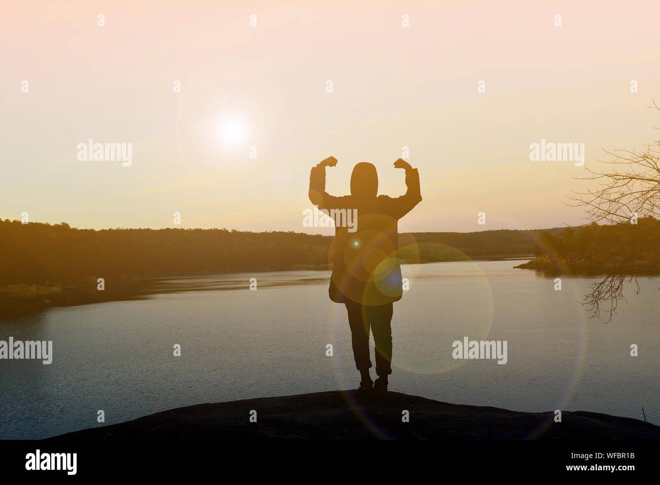 Silhouette Man Flexing Muscles On Rock Against Lake During Sunset Stock Photo