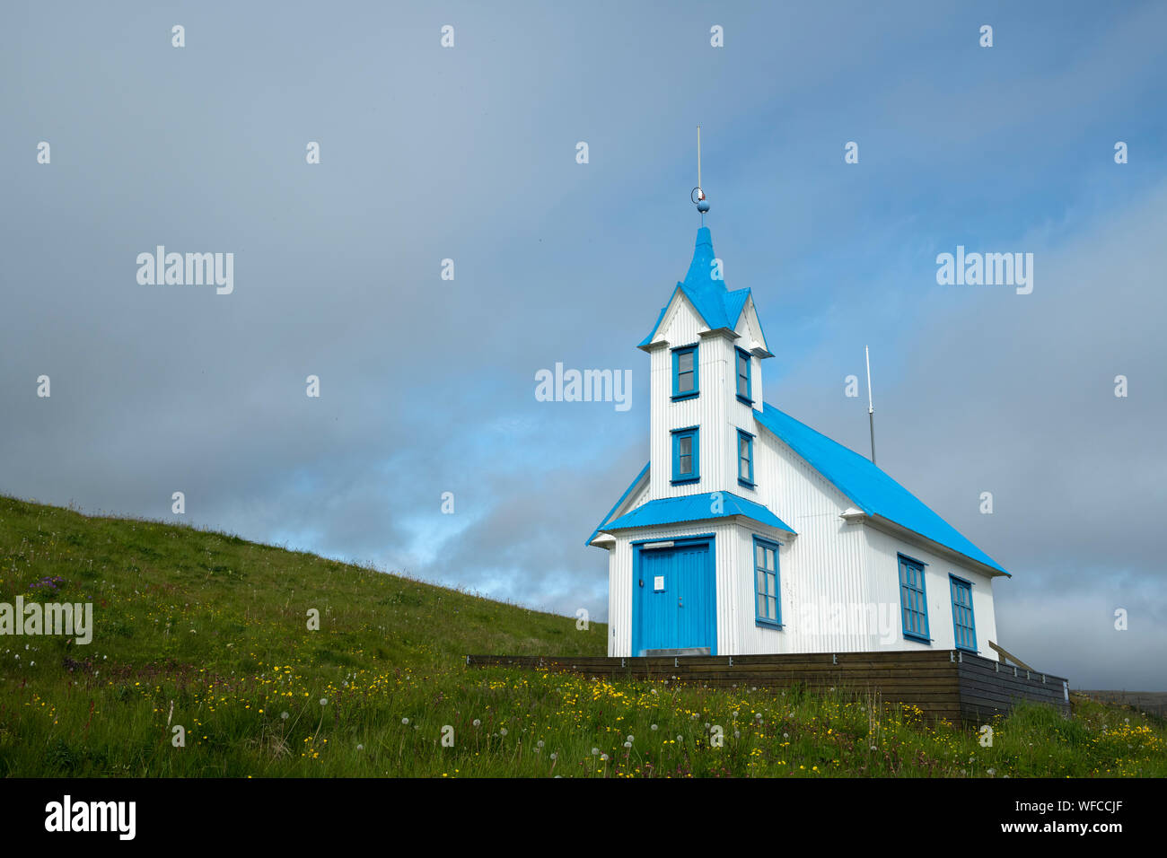 Stödvarfjördur blue and white converted church into a guesthouse on a small green grassy hill with soft coulds on a sunny summer day in Iceland Stock Photo