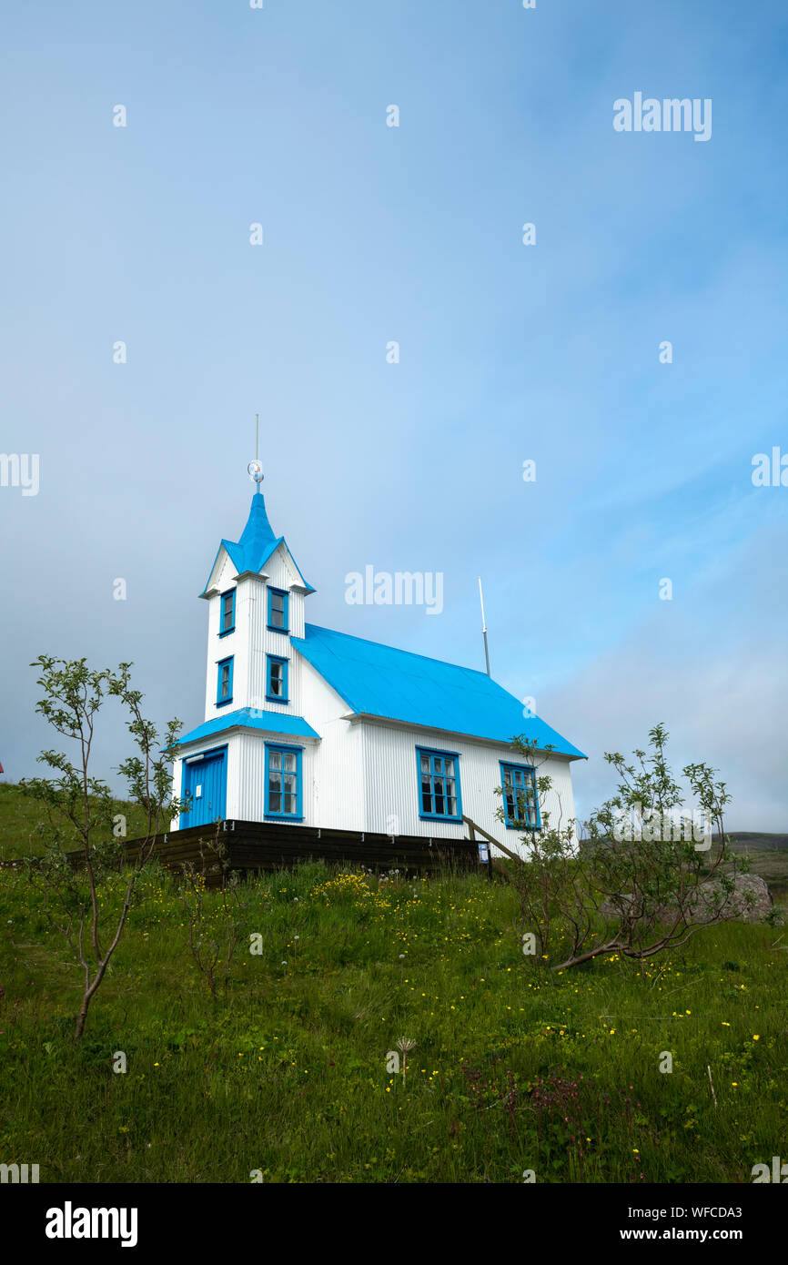 Stödvarfjördur blue and white converted church into a guesthouse on a small green grassy hill with soft coulds on a sunny summer day in Iceland Stock Photo