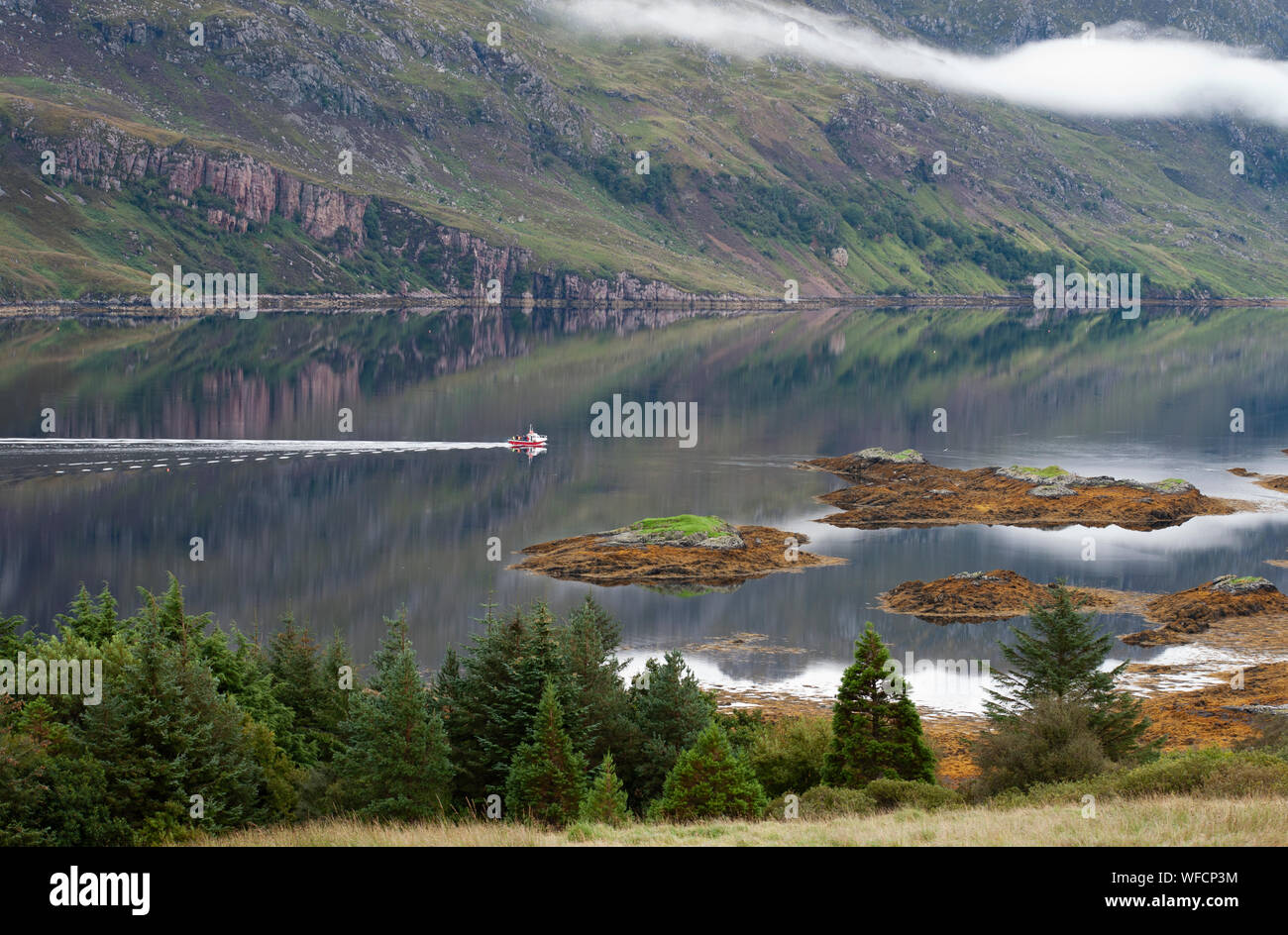 Loch with islands and red fishing boat moving across still water, Scottish Highlands, Scotland. Stock Photo