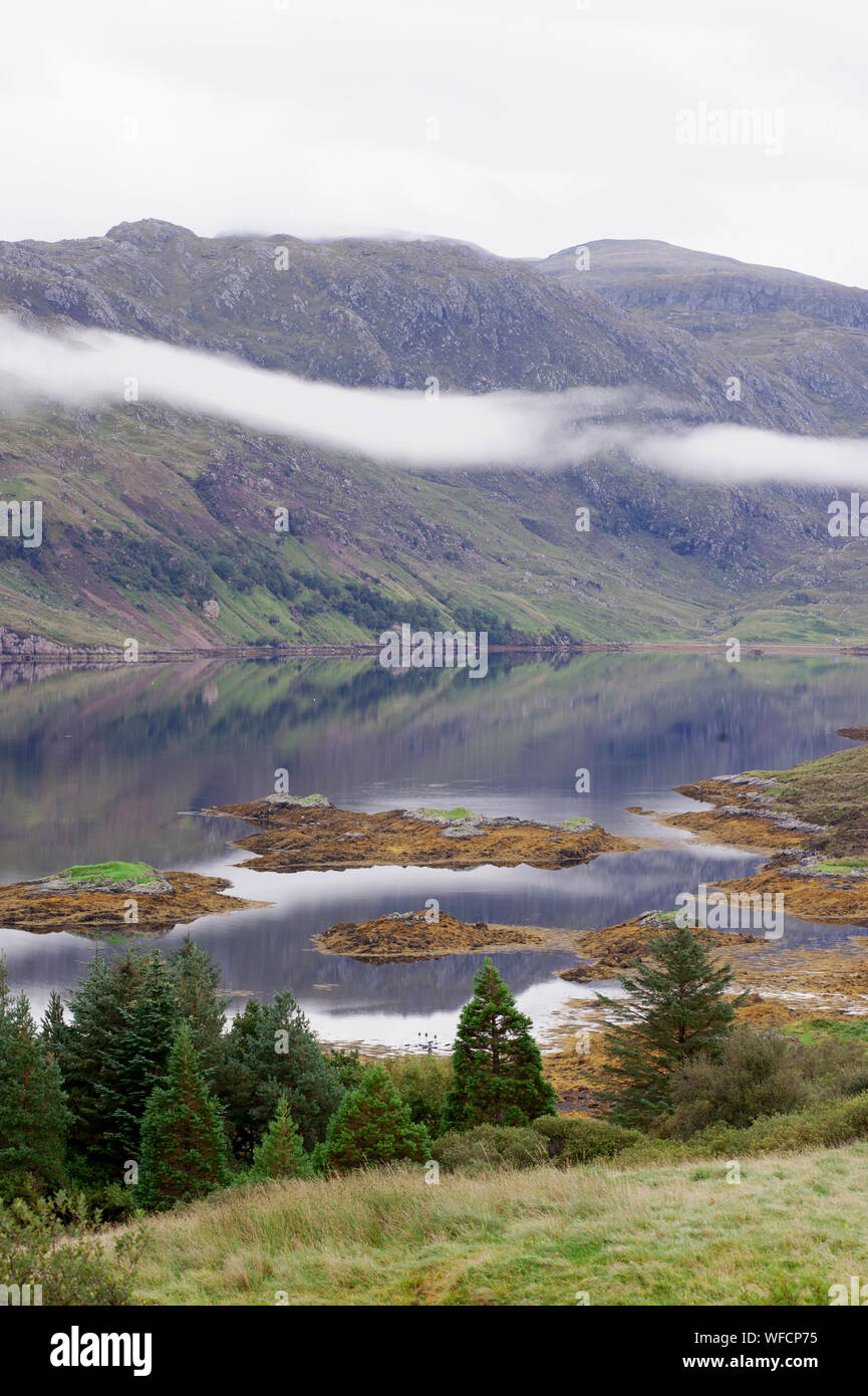 Loch with islands and red fishing boat moving across still water, Scottish Highlands, Scotland. Stock Photo