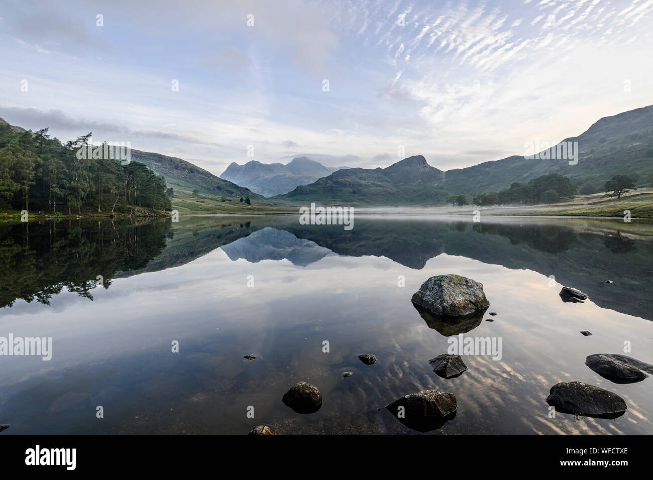 Mirror-like reflections of the Langdale Pikes in Blea Tarn early morning in late summer Stock Photo