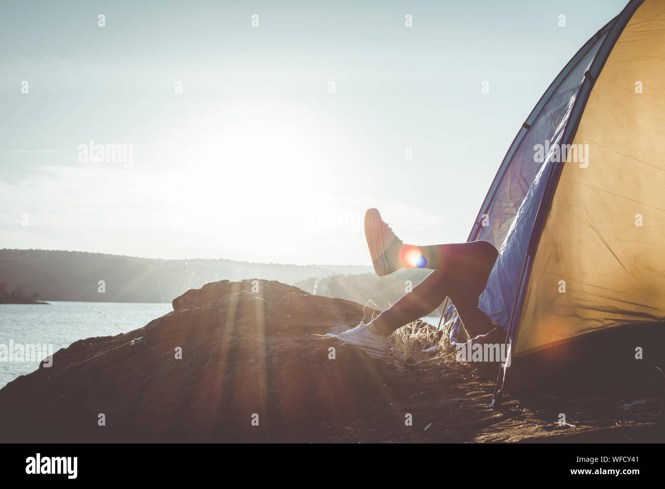Low Section Of Man Relaxing In Tent On Cliff By Sea During Sunny Day Stock Photo