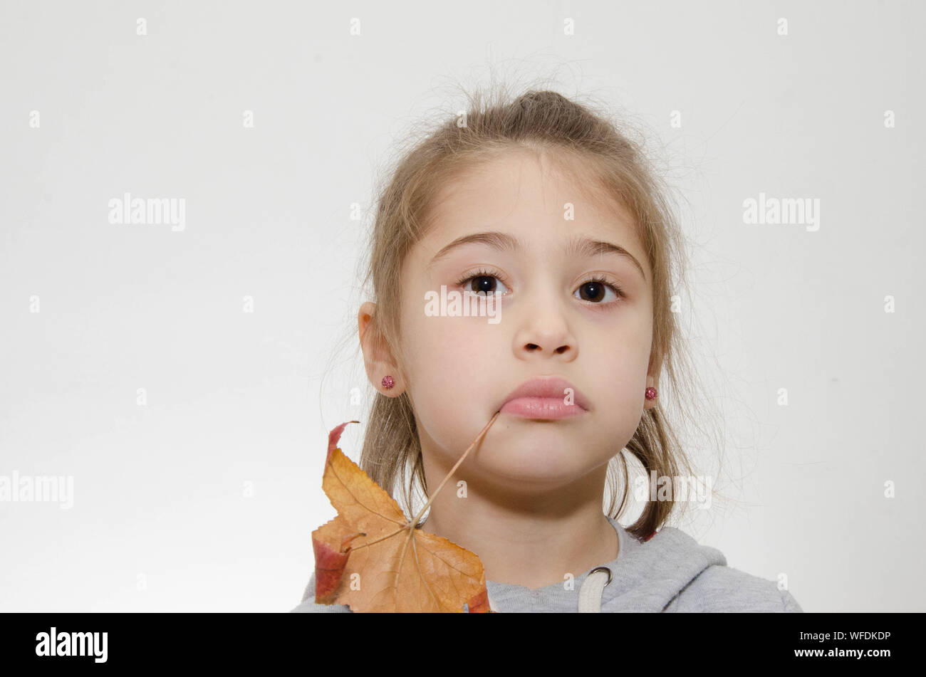 Close-up Portrait Of Cute Girl Biting Dry Leaf Stem Against White Background Stock Photo
