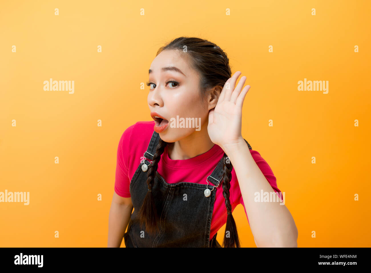 Young teenager Asian girl over isolated yellow background listening gossip by putting hand on the ear Stock Photo