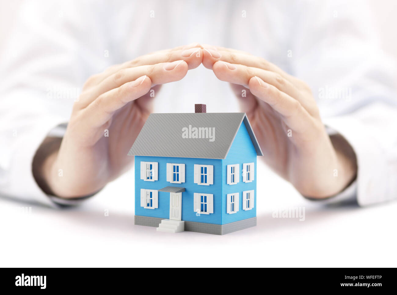Small blue house covered by hands Stock Photo