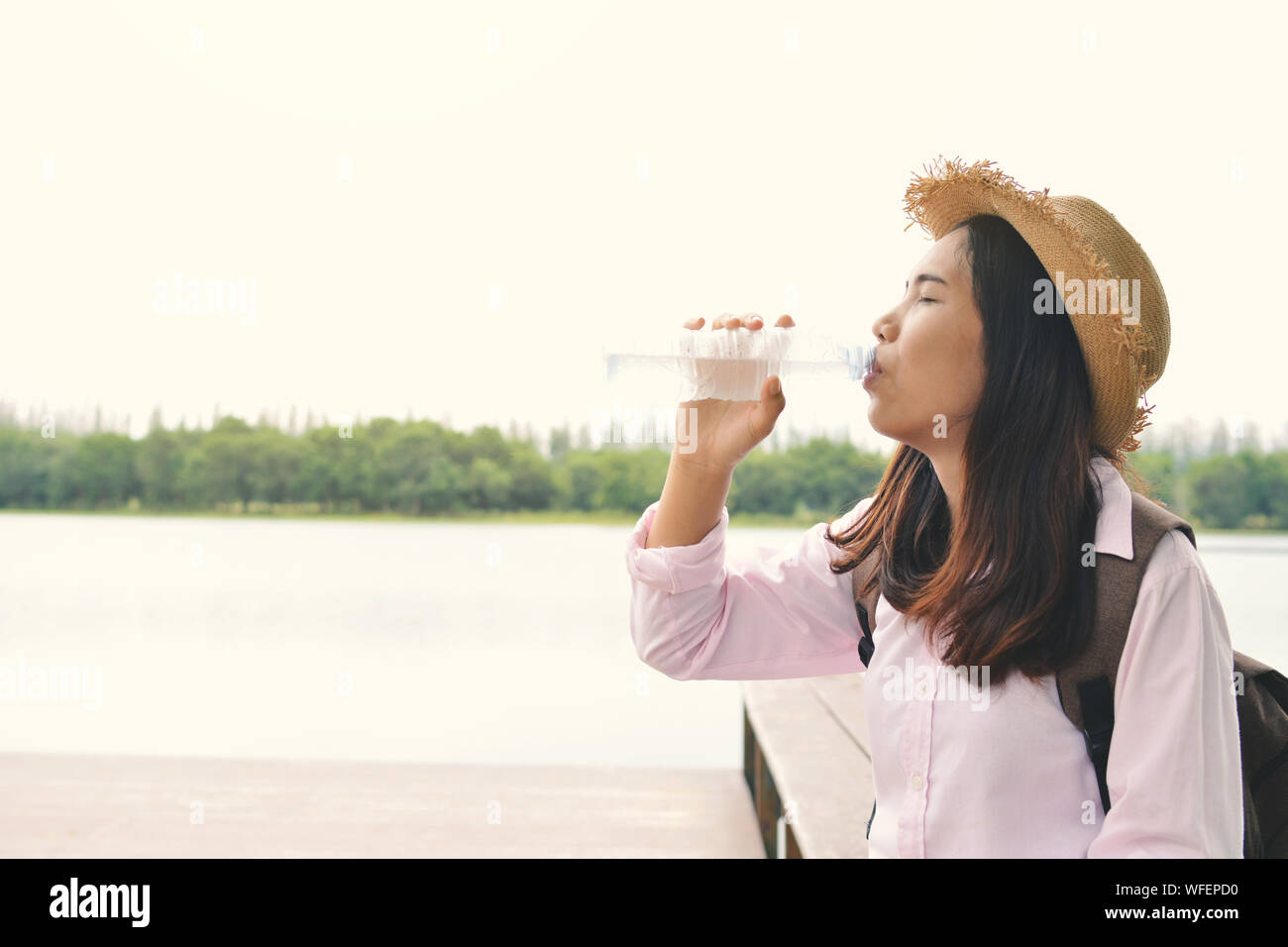 Thirsty Young Woman Drinking Water At Lakeshore Against Clear Sky Stock Photo