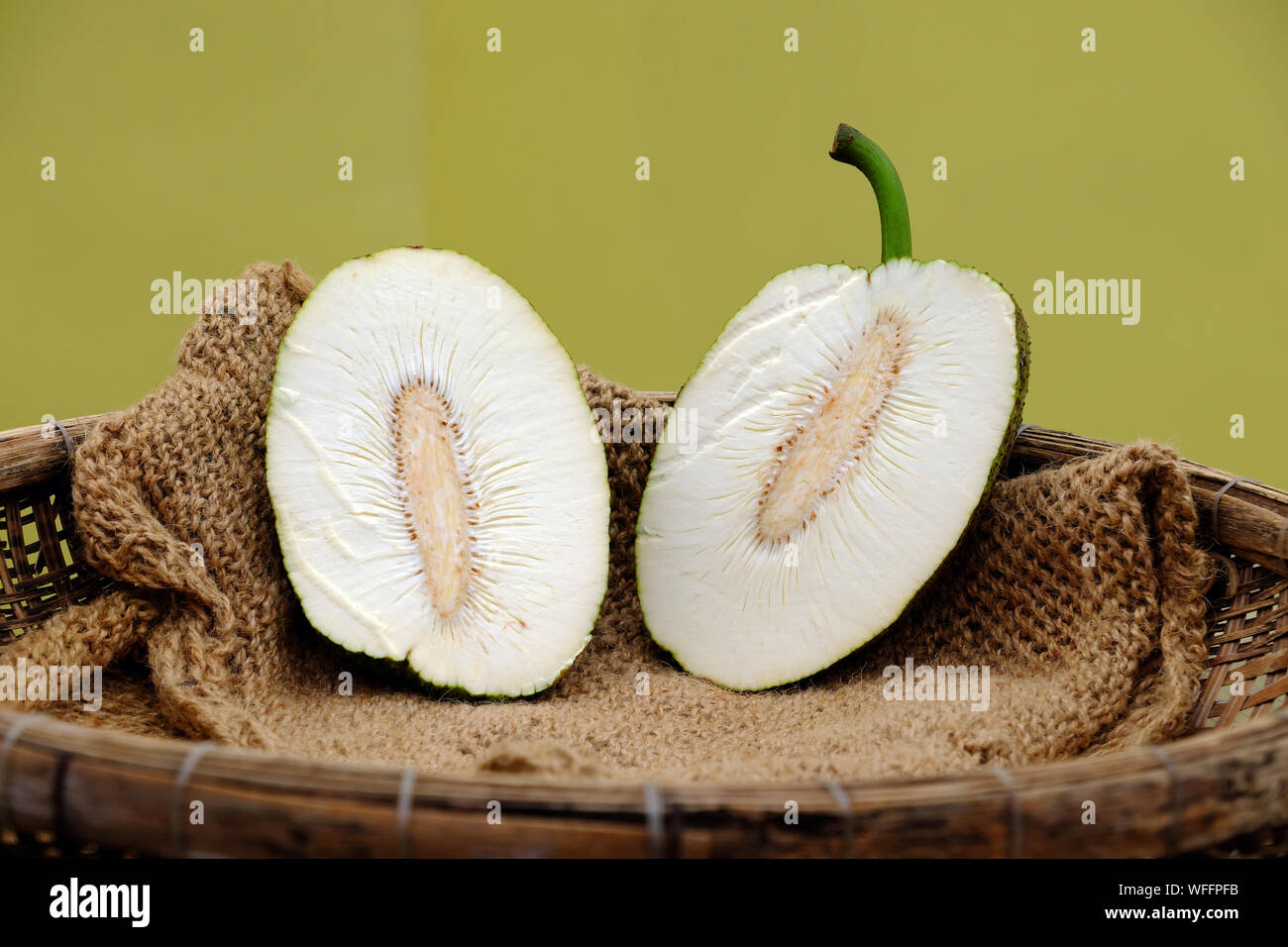 Breadfruit cut in half on burlap in bamboo basket on yellow background, Vietnamese healthy vegetarian dish Stock Photo