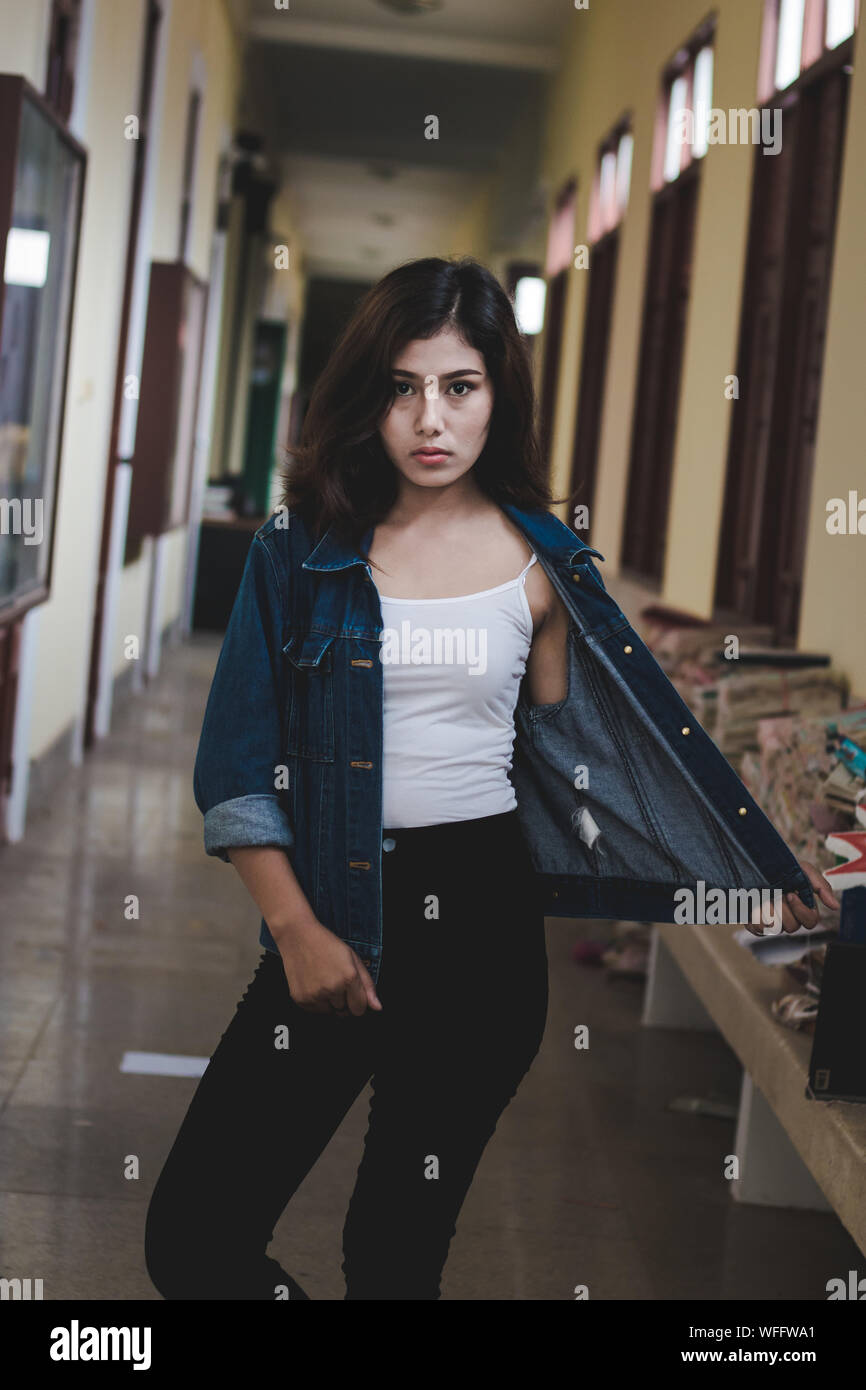 Portrait Of Confident Young Woman Wearing Denim Jacket Standing In Corridor Stock Photo