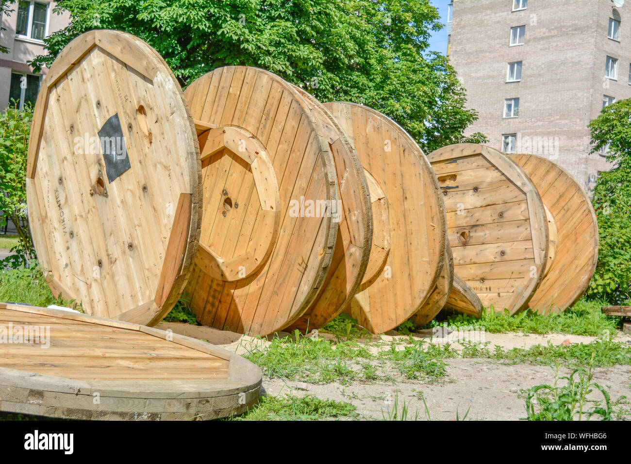 Large broken empty coils and reels with wooden cable drums, stacked on an  open street area with sand and grass in the city park near to the houses  Stock Photo - Alamy