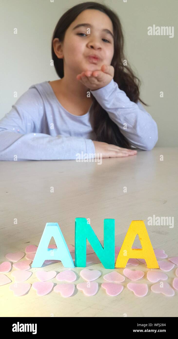 Portrait Of Cute Girl Blowing Kiss Towards Alphabet On Table At Home Stock Photo