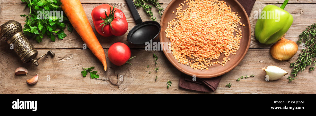 Lentil soup ingredients: red lentil, seasonal organic vegetables on wooden table, top view, banner. Cooking autum, winter seasonal soups and dishes. Stock Photo