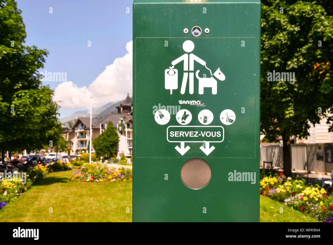 A dog waste bag dispenser in a public park of Chamonix-Mont-Blanc with blooming bedflowers and trees in the background in summer, Haute Savoie, France Stock Photo